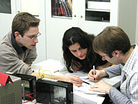 Studierende im Fach Physik rechnen neben elektrischem Schaltkreis