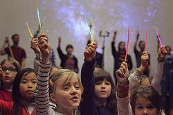 Kinder die ihren Arm mit etwas leuchtendem in die Luft strecken.