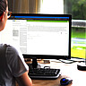 Das Foto zeigt eine Frau am Schreibtisch mit PC Bildschirm.