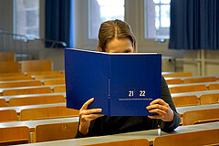 Frau sitzt in einem Hörsaal der Hochschule. Sie liest die 2021-2022-Ausgabe des Jahresberichts.