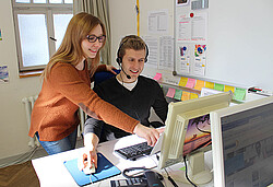 Frau die einem jungen Mann etwas auf einem Computer Bildschirm zeigt.