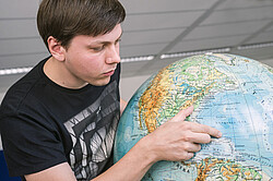 Junge der auf eine Insel auf einem Globus zeigt.
