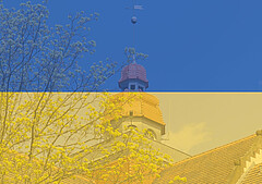 Das Symbolbild zeigt im Hintergrund den Turm des Altbaus der Hochschule. Darüber liegt leicht transparent die ukrainische Flagge.