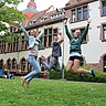 Das Foto zeigt drei springende Studierende vor dem Altbau der Hochschule.