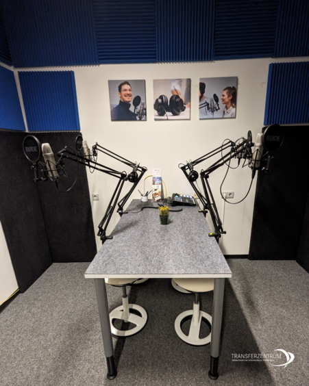 Das Foto zeigt das Podcast-Studio mit einem Tisch und vier Mikrofonen