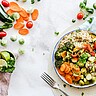 Auf einem weißen Tischtuch liegen verschiedene Gemüsesorten und ein Teller mit einem gemüsereichen vegetarischen Essen ist abgebildet