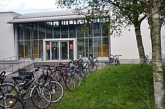 Das Bilder zeigt den Eingang des Hörsaalgebäudes der Pädagogischen Hochschule Heidelberg von außen. Davor sind zahlreiche Fahrräder abgestellt.
