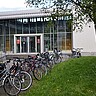 Das Bilder zeigt den Eingang des Hörsaalgebäudes der Pädagogischen Hochschule Heidelberg von außen. Davor sind zahlreiche Fahrräder abgestellt.