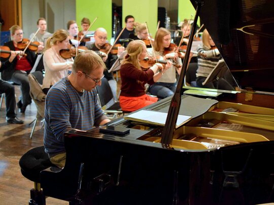 Mehrere Studierende spielen Streichinstrumente, im Vordergrund sitzt eine Person am Flügel.