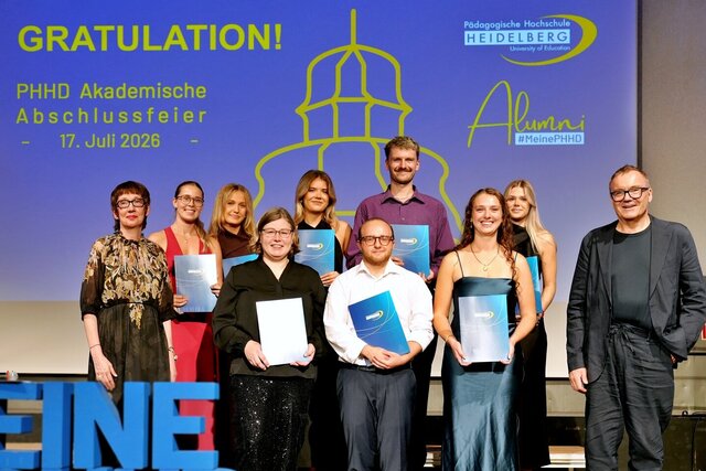 Zu sehen sind Absolvent:innen der PHHD, die sich mit ihren Urkundenmappen auf der Bühne zum Gruppenfoto aufgestellt haben.
