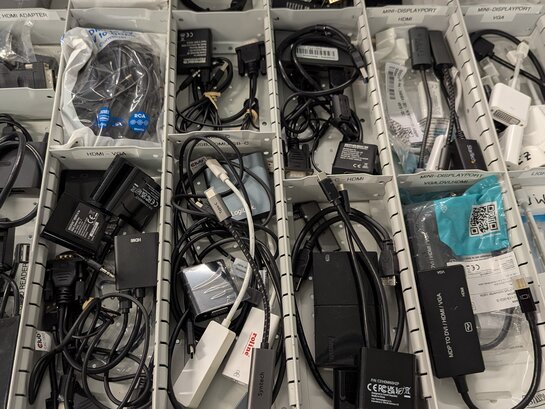 Foto einer Schublade mit Adaptern für Displayport, HDMI, LAN, USB, VGA und mehr. 