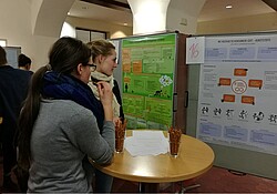zwei Frauen die vor den Präsentationen der Arbeiten aus dem Übergreifenden Studienbereich in der Aula stehen.