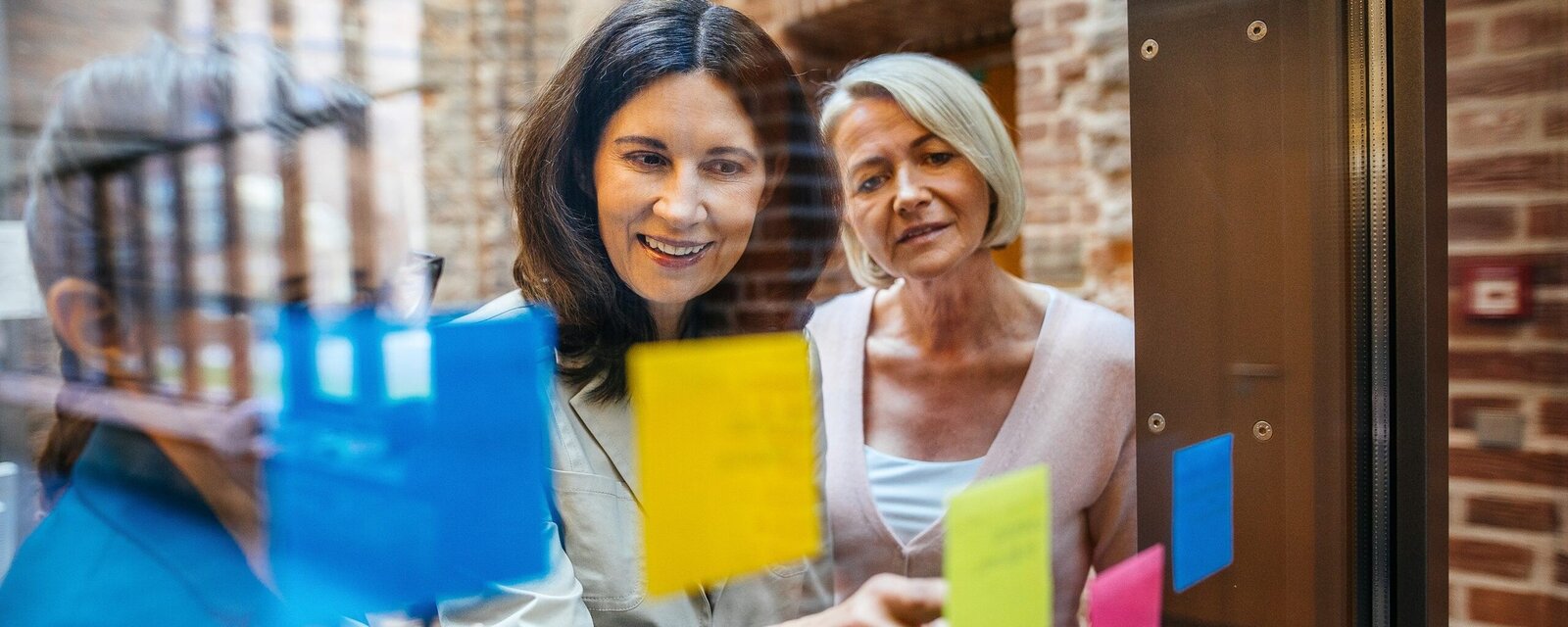 Personen schauen durch eine Fensterscheibe auf Post its