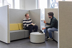 Das Symbolbild zeigt zwei junge Männer, die sich sitzend unterhalten. Das Bild wurde im Transferzentrum der Hochschule aufgenommen.