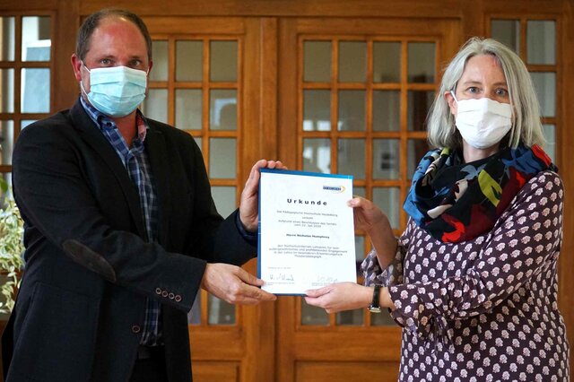 Vera Heyl überreicht Nicholas Humphrey seine Urkunde. Beide tragen corona-bedingt eine Maske.