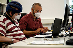 zwei Männer mit Maske vorm PC