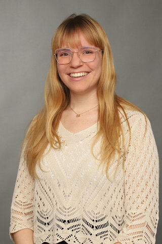 Zu sehen ist ein Portraitfoto von Alumna Hannah Lene Schreiber vor einem dunklen Hintegrund