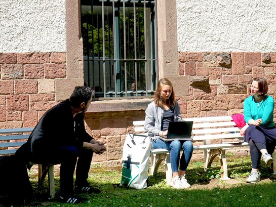 DasBild zeigt Dr. Klemens Ketelhut, Svenja Woitt und Sarah Maier. Sie sitzen auf Bänken im Innenhof des Altbaus der Pädagogischen Hochschule Heidelberg.