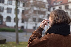 Studentin vor dem Altbau der PH beim Aufsetzen einer medizinischen Maske. Copyright Pädagogische Hochschule Heidelberg