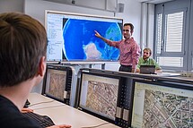 Raum mit Personen und digitalen Medien, welche geografische Karten zeigen. Copyright Pädagogische Hochschule Heidelberg