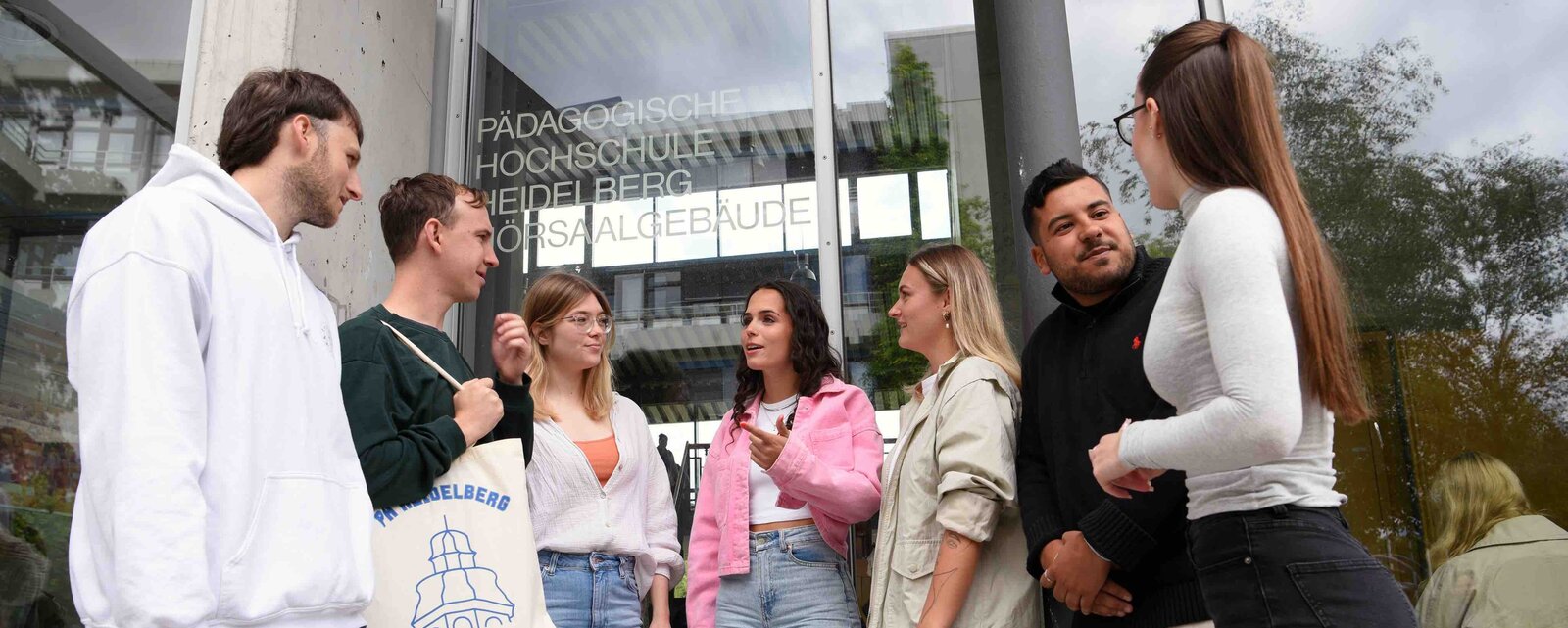 Eine Gruppe von Studierenden steht vor dem Hörsaalgebäude der Pädagogischen Hochschule Heidelberg und unterhält sich.