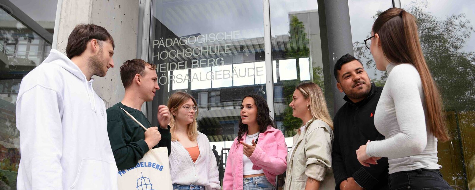 Eine Gruppe von Studierenden steht vor dem Hörsaalgebäude der Pädagogischen Hochschule Heidelberg und unterhält sich.