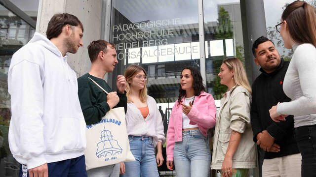 Eine Gruppe von Studierenden steht vor dem Hörsaalgebäude der Pädagogischen Hochschule Heidelberg und unterhält sich.