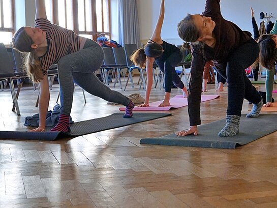 Abgebildet sind Menschen beim Yoga in der Altbau-Aula der PH Heidelberg. Ein Bewegungsangebot, das gesundes Arbeiten ermöglichen soll.