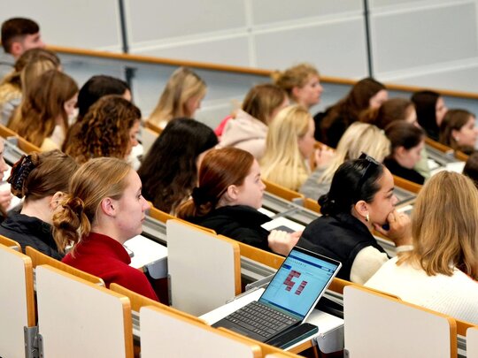 Studierende sitzen im Hörsaal, ihr Blick ist nach vorne gerichtet.