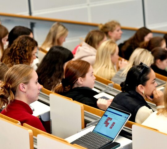 Studierende sitzen im Hörsaal, ihr Blick ist nach vorne gerichtet.