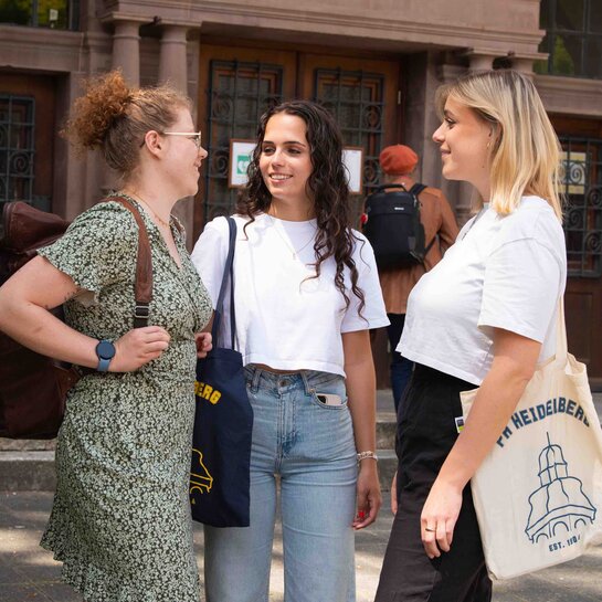 Zu sehen sind drei junge Studentinnen die in Heidelberg studieren und vor der Pädagogischen Hochschule stehen.