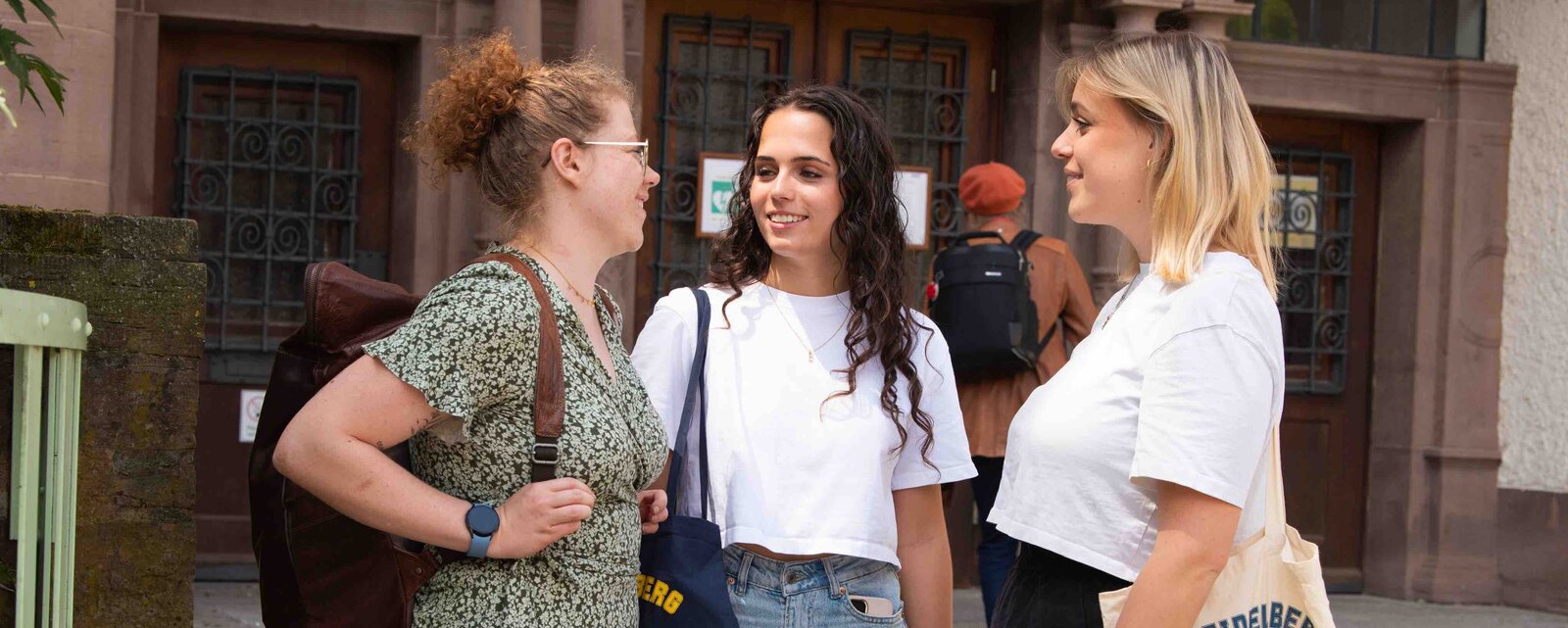 Drei Studentinnen unterhalten sich vor den Haupteingang des Altbaus der Pädagogischen Hochschule Heidelberg.