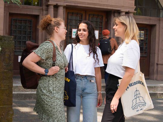 Drei Studentinnen unterhalten sich vor den Haupteingang des Altbaus der Pädagogischen Hochschule Heidelberg.