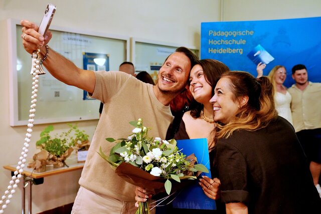 Zu sehen sind drei Personen, die ein Selfie vor der PHHD-Messerückwand machen.
