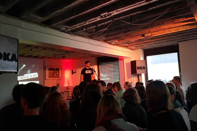 Zu sehen sind Menschen im Café Leitstelle beim Science Slam von Transfer Together 2018.