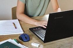 Das Bild zeigt einen Schreibtisch auf dem ein Laptop liegt und einer Person daran arbeitet. Copyright Pädagogische Hochschule Heidelberg