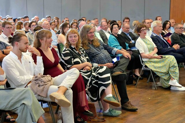 Zu sehen ist das Publikum aus leichter Seitenansicht.