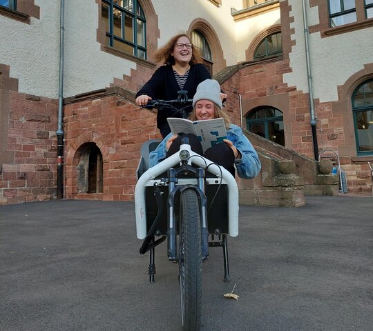 Zu sehen ist PH-Studentin Paula im Lastenrad mit Chiara am Steuer, wie sie im Innenhof des Altbaus der PH Heidelberg fahren.