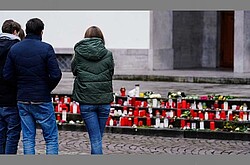 Trauernde, welche auf viele rote Gedenkkerzen schauen.