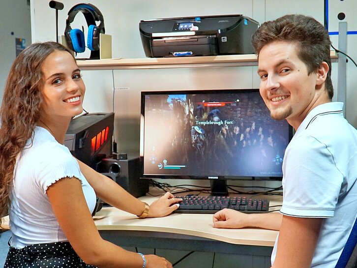 Studenten sitzen an dem Gamer-PC im Medienlabor und schauen in die Kamera.