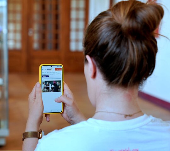 Frau hält Handy auf dem man das Campus-Portal der Pädagogischen Hochschule Heidelberg sieht