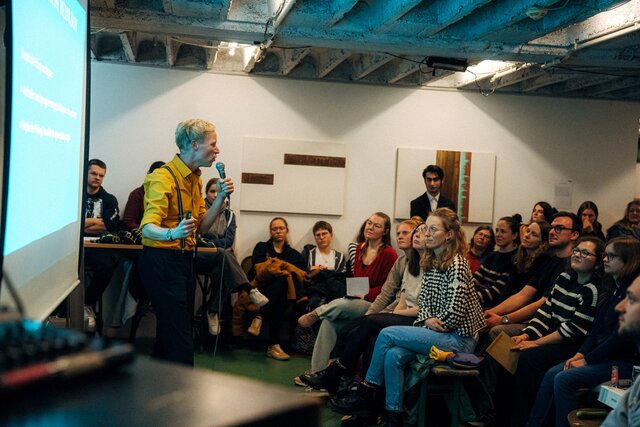 Zu sehen ist Tom Wellmann und das Publikum beim Science Slam der PH Heidelberg 2024.