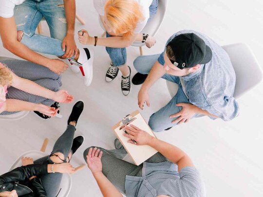 Eine Gruppen sitzt im Stuhlkreis. Das Foto ist von oben aufgenommen, sodass man keine Gesichter erkennt. 
