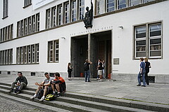 Das Bild zeigt die Neue Universität von außen. Davor sitzen und stehen eine Vielzahl von Studierenden.
