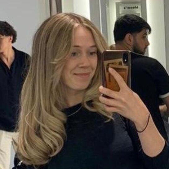 Mona macht ein Spiegel-Selfie. Sie hat lange blonde Haare und einen schwarzen Pulli an.