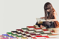 lesendes gezeichnetes Mädchen was auf einem Bücherberg sitzt.