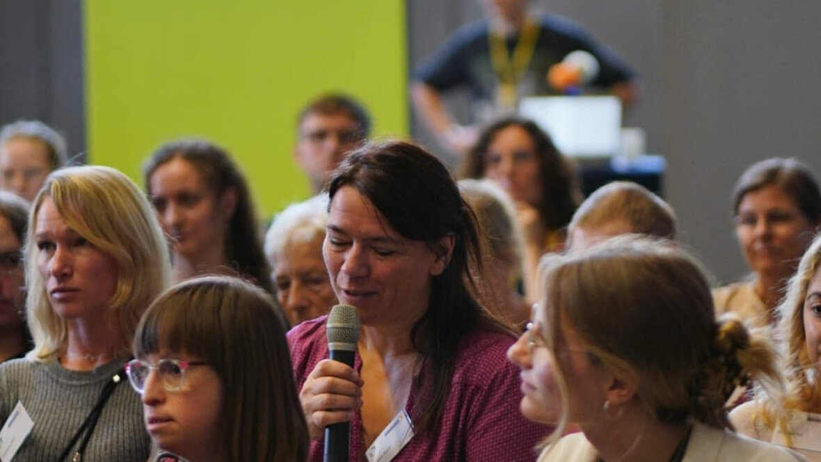 Das Bild zeigt einen Teil des Publikums der Podiumsdiskussion. Eine Frau stellt eine Frage.