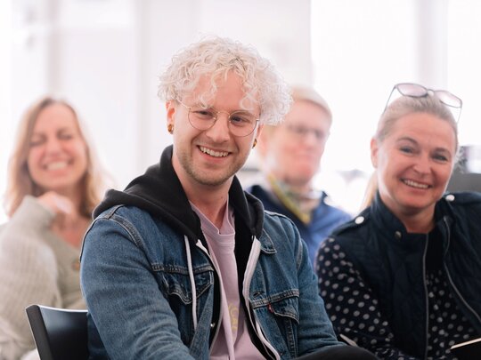 Vier Menschen auf Stühlen die freundlich lächeln