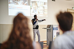 Referierenden auf der Bühne in der Aula im Altbau. 