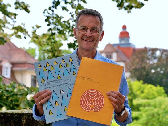 Das Bild zeigt Professor Dr. Markus Lang, der zwei Hefte mit Braille-Schrift in den Händen hält.